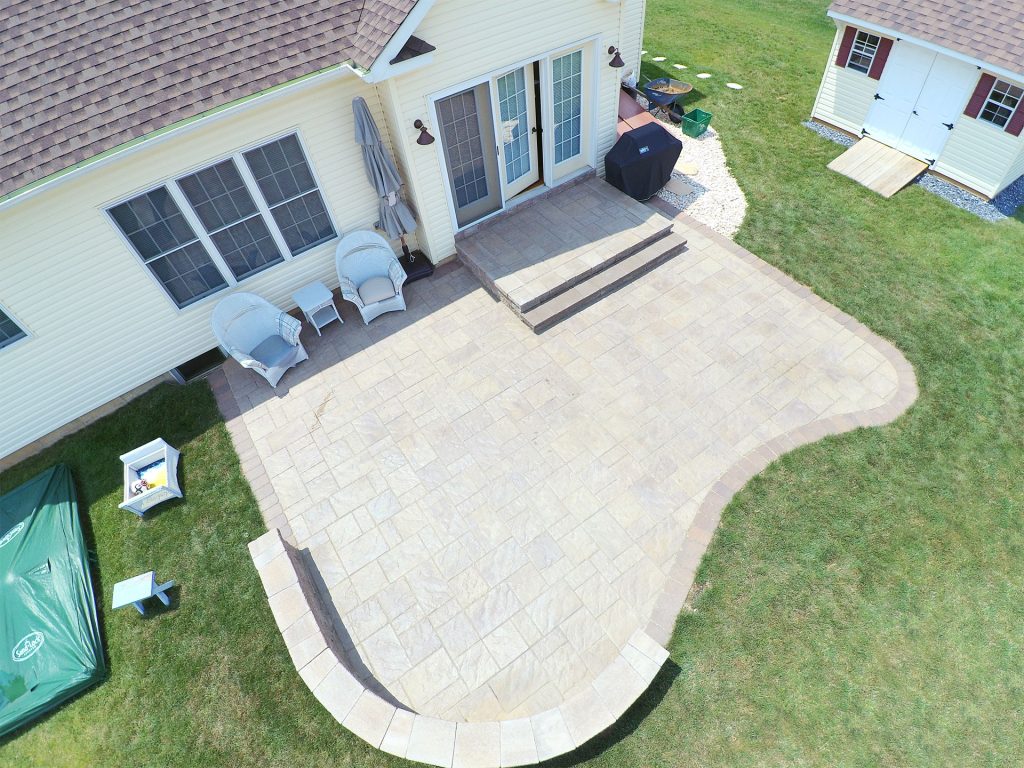 aerial view of a home's backyard with a stone patio and retaining wall